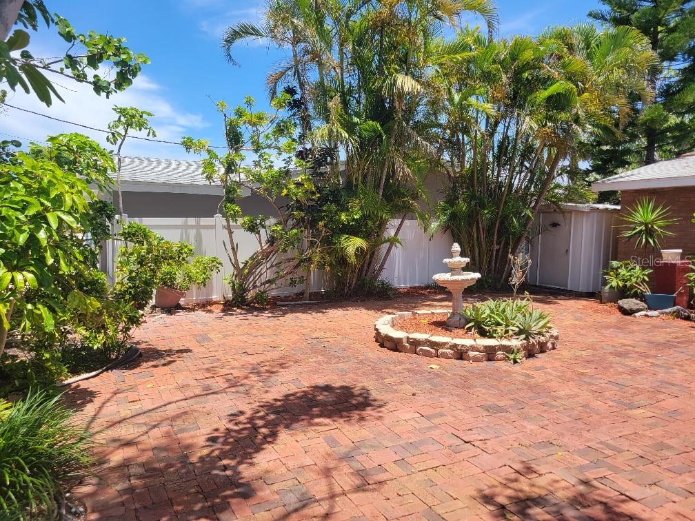 A brick patio features a central tiered fountain surrounded by palm trees and a fence — 315 S TESSIER DRIVE, ST PETE BEACH, FL