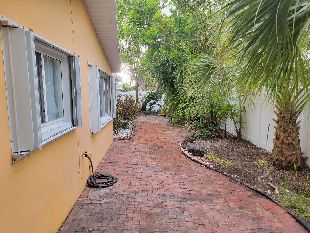 A brick walkway runs alongside a yellow house with white shutters and a privacy fence — 315 S TESSIER DRIVE, ST PETE BEACH, FL