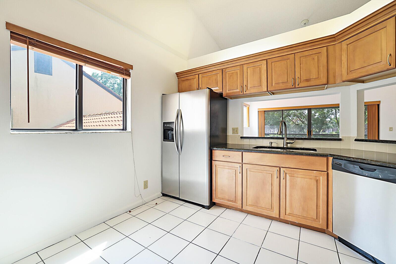 A kitchen with wood cabinets, stainless steel appliances, black countertops, and white tile flooring — 9 Vía De Casas Sur # 203, Boynton Beach FL 33426, BOYNTON BEACH, FL