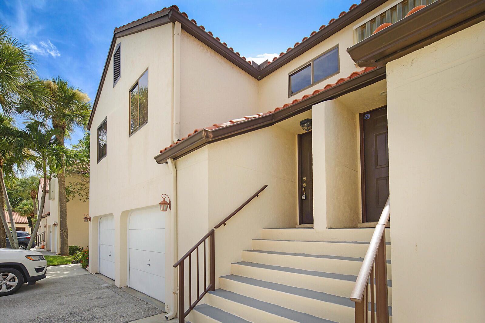 A two-story building with a beige stucco exterior, two garage doors, and a staircase entrance — 9 Vía De Casas Sur # 203, Boynton Beach FL 33426, BOYNTON BEACH, FL