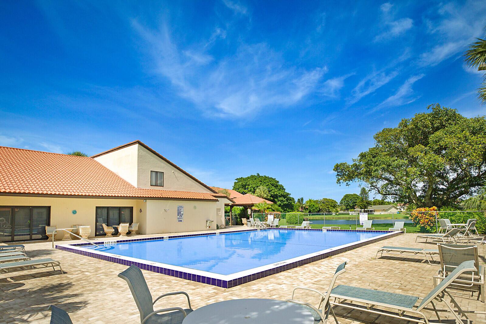 A rectangular swimming pool sits on a paved patio next to a tan building — 9 Vía De Casas Sur # 203, Boynton Beach FL 33426, BOYNTON BEACH, FL
