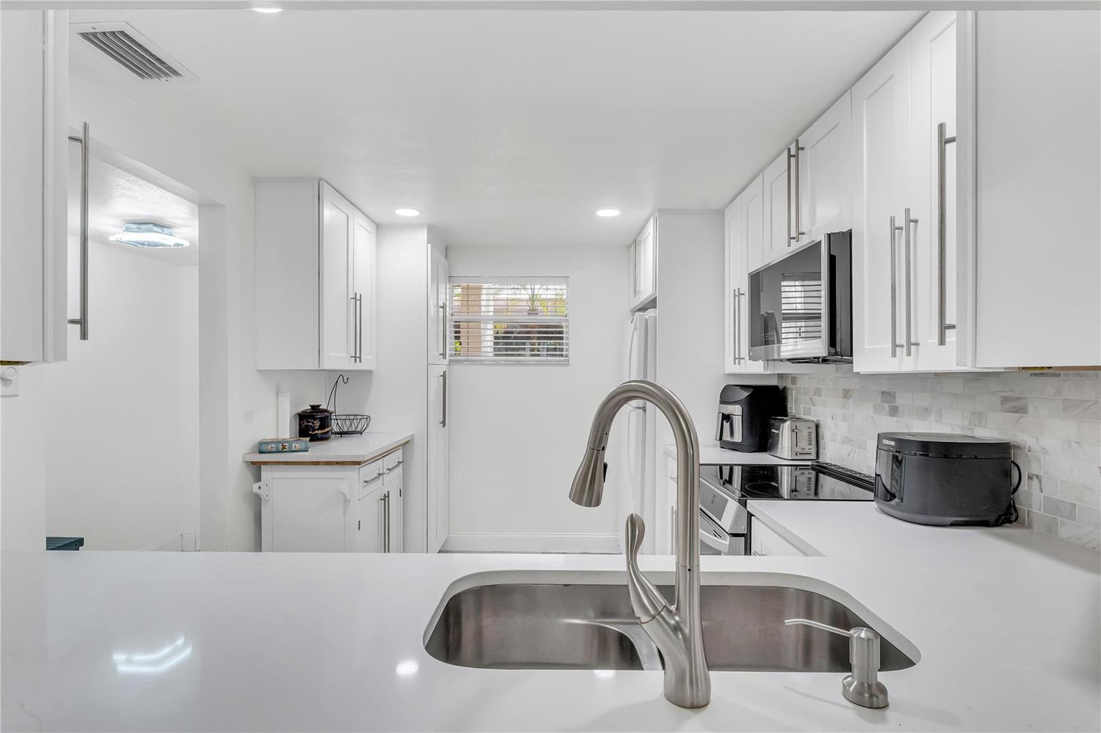A bright white kitchen features stainless steel appliances, quartz countertops, and a double-basin sink — 3920 Inverrary Boulevard # C, Lauderhill FL 33319, LAUDERHILL, FL