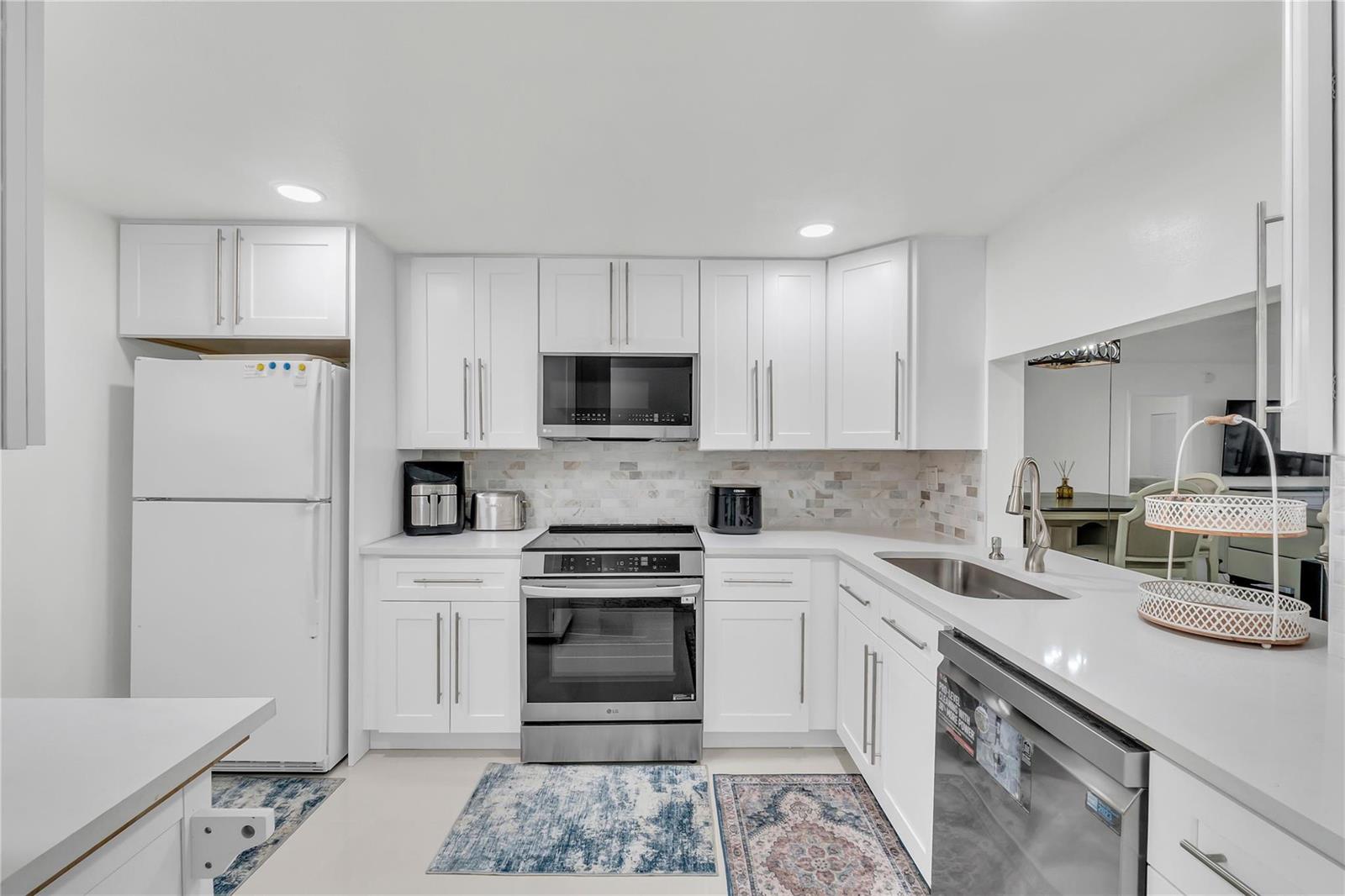 A white kitchen features stainless steel appliances, quartz countertops, and a tiled backsplash — 3920 Inverrary Boulevard # C, Lauderhill FL 33319, LAUDERHILL, FL