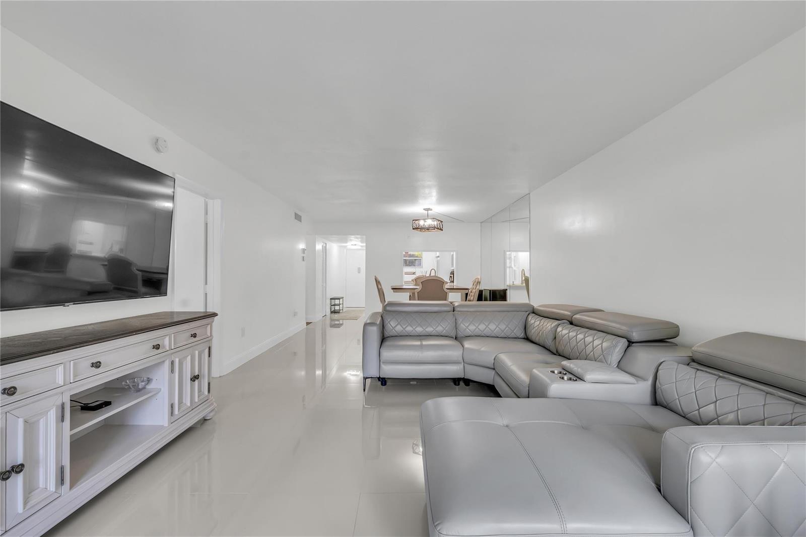 A living room features a large grey sectional sofa, a white media console, and tile flooring — 3920 Inverrary Boulevard # C, Lauderhill FL 33319, LAUDERHILL, FL