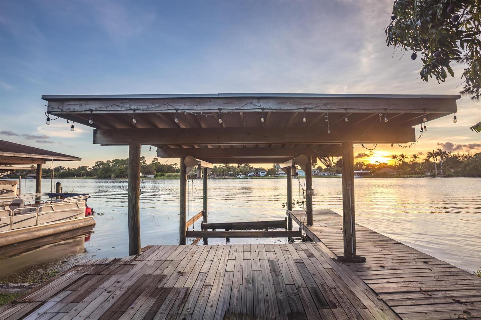 A wooden boat dock with a covered slip sits on a calm waterfront at sunset — 6563 Paul Mar Drive, Lake Worth FL 33462, LAKE WORTH, FL