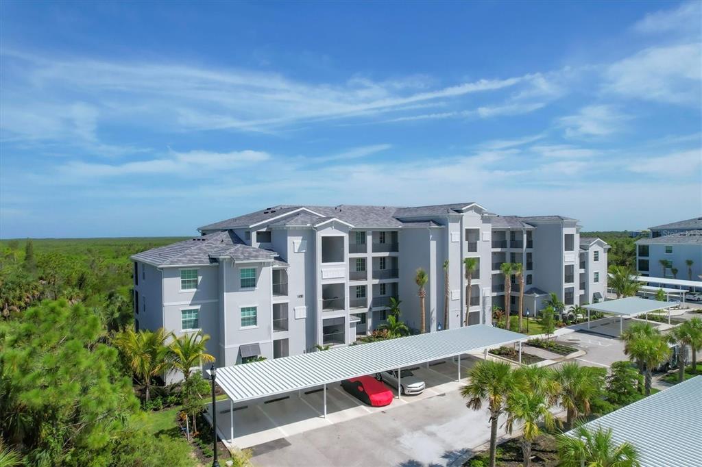An aerial view of a multi-story apartment building with covered parking and surrounding palm trees — 14161 HERITAGE LANDING BOULEVARD UNIT 1123, PUNTA GORDA, FL