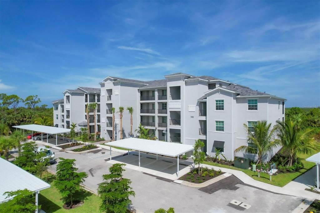 An exterior view of a multi-story apartment building with covered parking spaces and palm trees — 14161 HERITAGE LANDING BOULEVARD UNIT 1123, PUNTA GORDA, FL