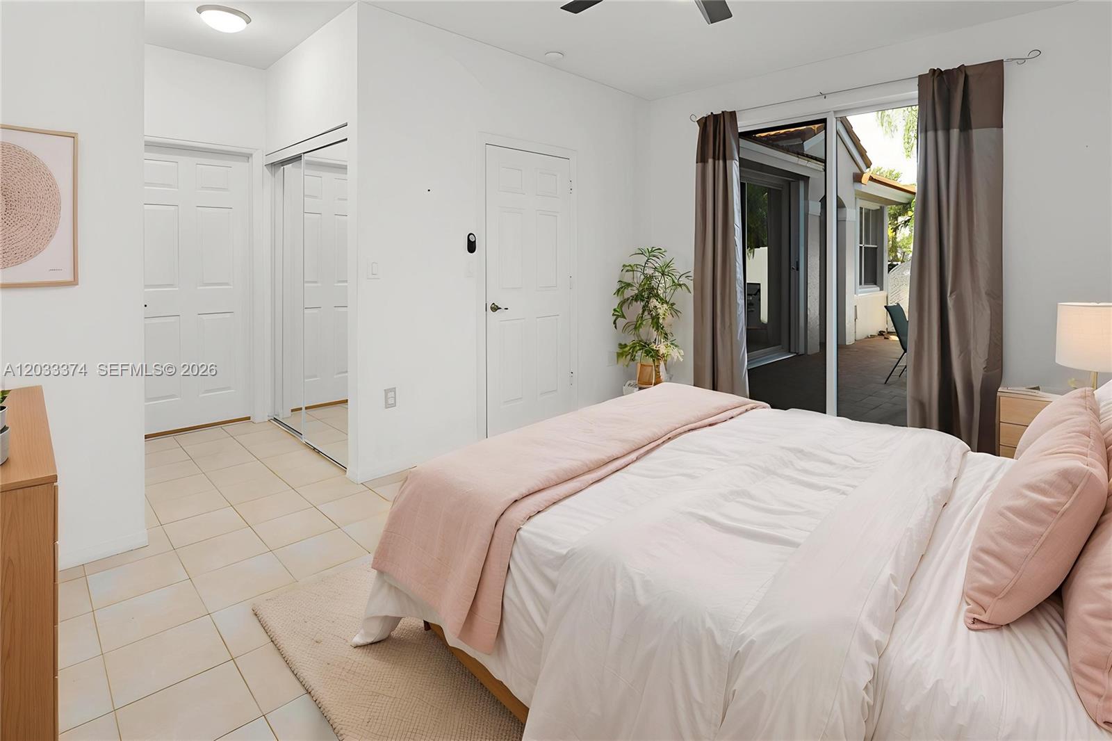 A bedroom features a bed with pink bedding, tiled floors, mirrored closet doors, and sliding doors — 1521 Seagrape Way, Hollywood FL 33019, HOLLYWOOD, FL