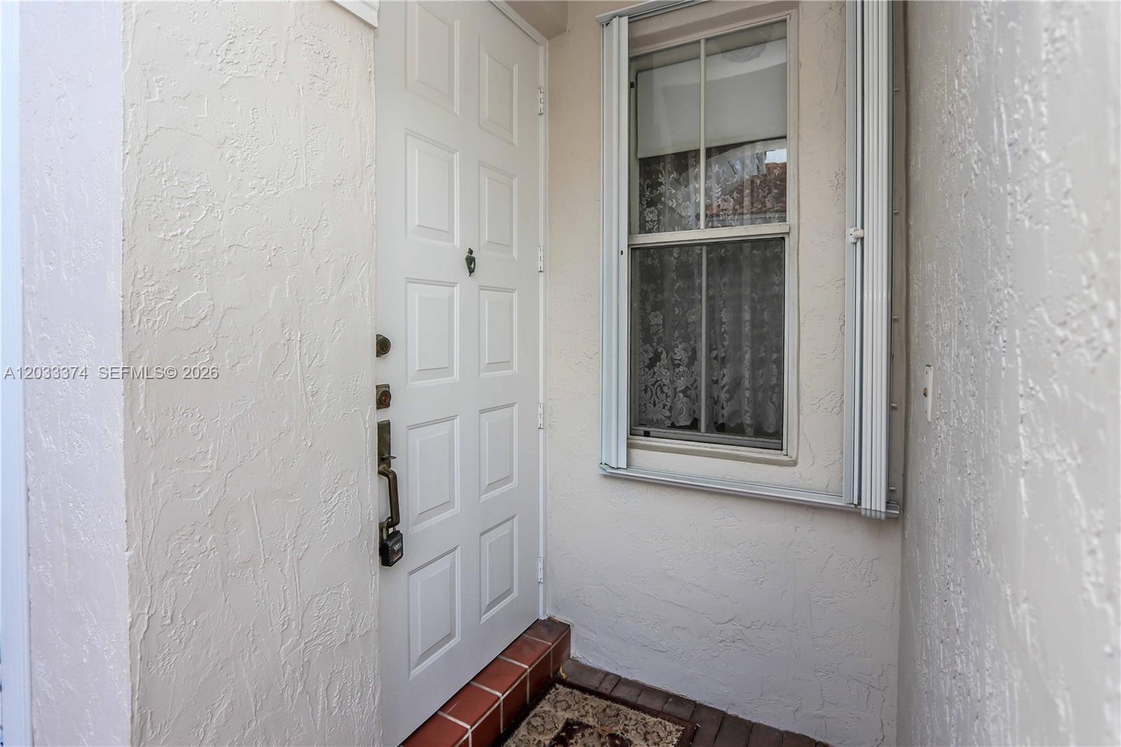 A white front door with a lockbox sits next to a window with shutters — 1521 Seagrape Way, Hollywood FL 33019, HOLLYWOOD, FL