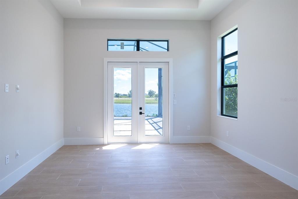 An empty room with light tile floors, white walls, double glass doors, and a water view — 312 BLUE PEARL CT., SARASOTA, FL