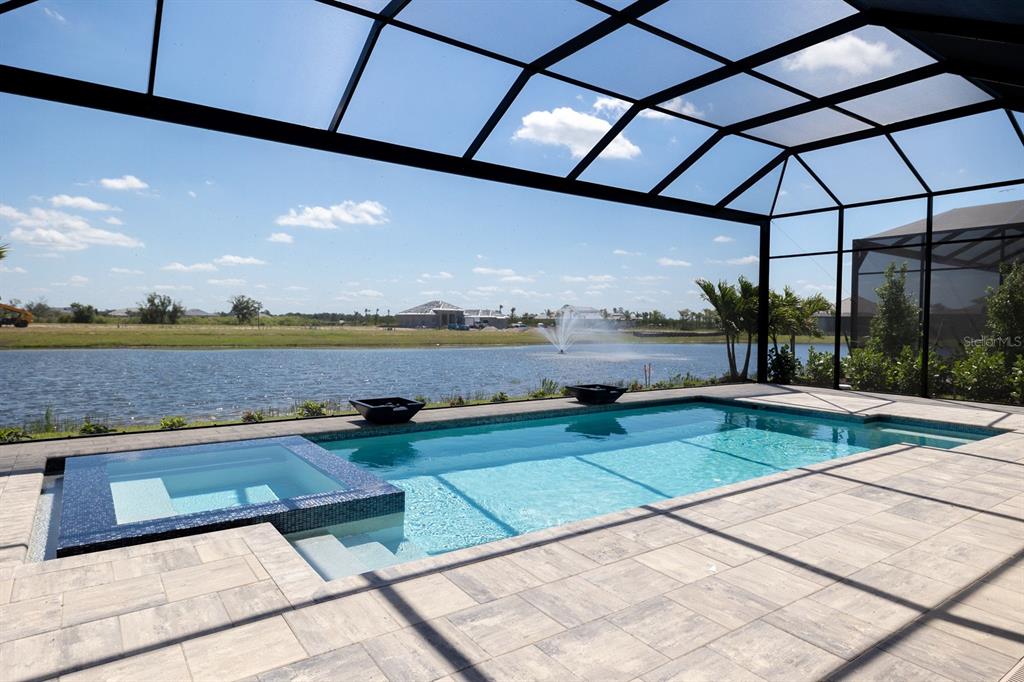 A screened-in pool and spa overlook a lake with a fountain under a blue sky — 312 BLUE PEARL CT., SARASOTA, FL