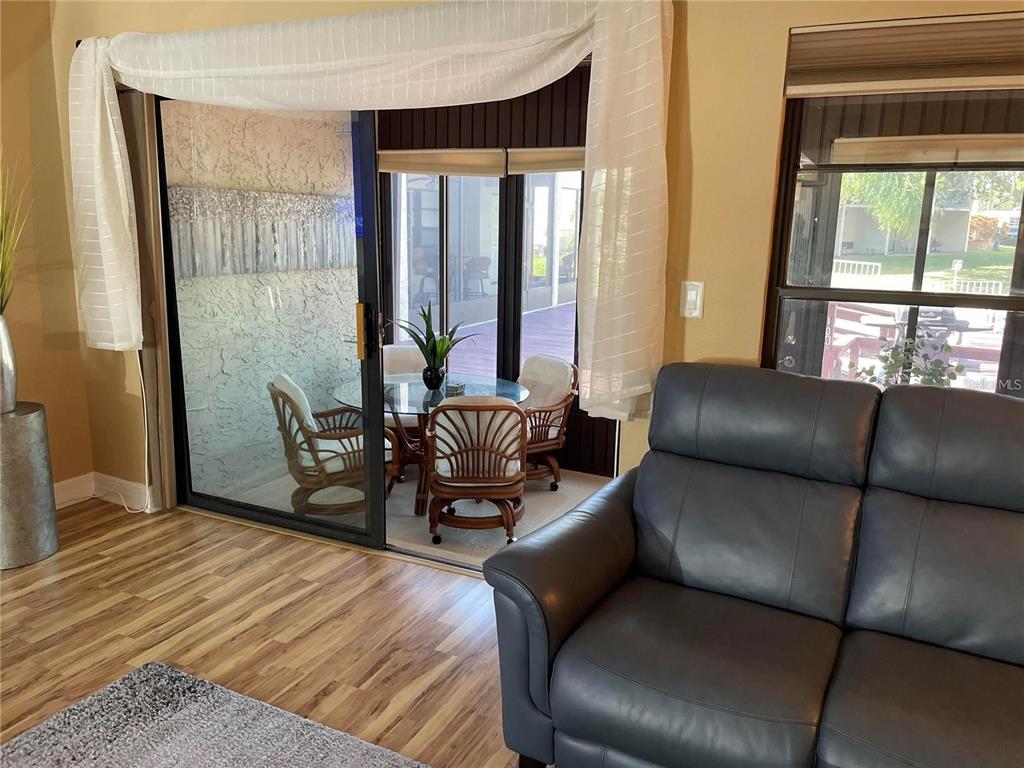 A living room with wood-look flooring leads through a sliding glass door to a patio — 2571 CYPRUS DRIVE UNIT 1-104, PALM HARBOR, FL