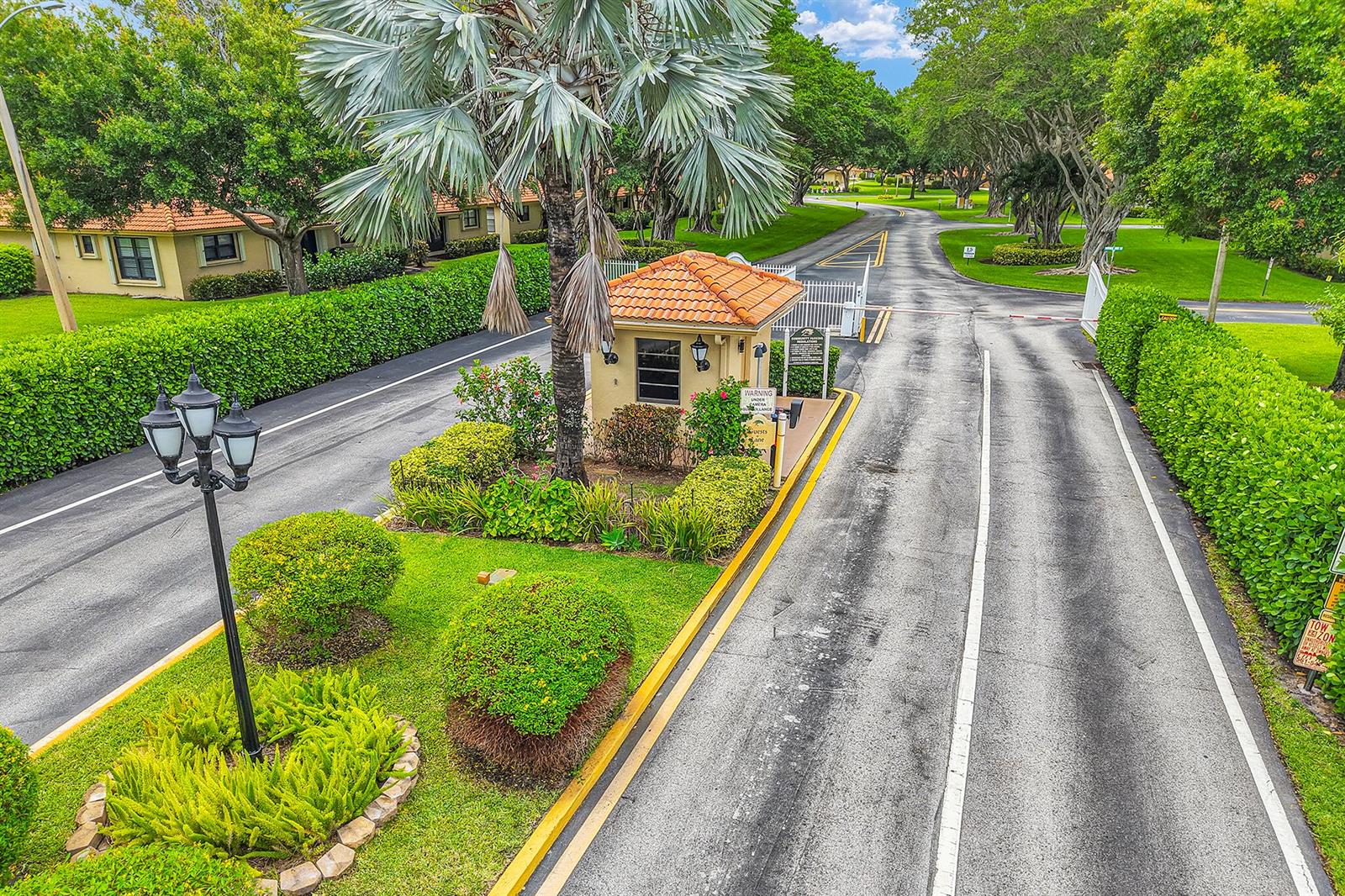 An aerial view shows a gated community entrance with a guardhouse, palm tree, and landscaping — 4450 Nutmeg Tree Lane # A, Boynton Beach FL 33436, BOYNTON BEACH, FL