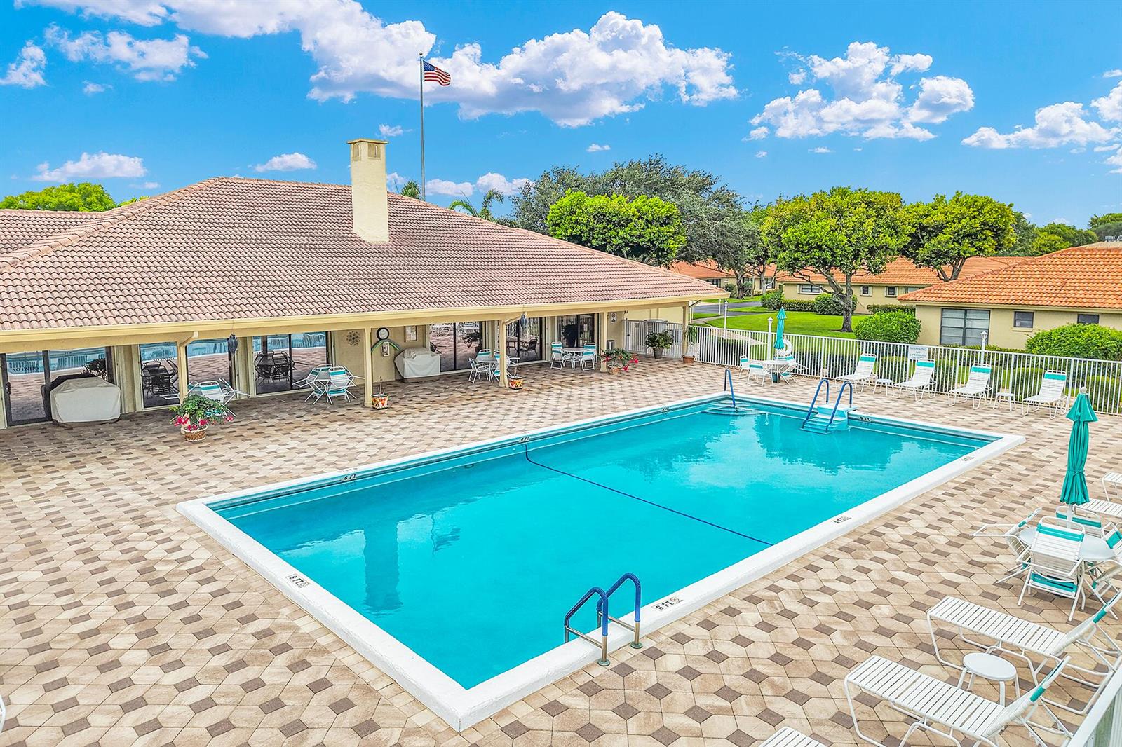 A rectangular swimming pool sits on a paved patio beside a building with a tiled roof — 4450 Nutmeg Tree Lane # A, Boynton Beach FL 33436, BOYNTON BEACH, FL