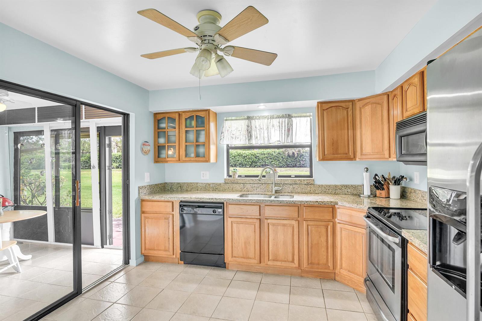 A kitchen with light blue walls, oak cabinets, granite countertops, and a ceiling fan — 4450 Nutmeg Tree Lane # A, Boynton Beach FL 33436, BOYNTON BEACH, FL