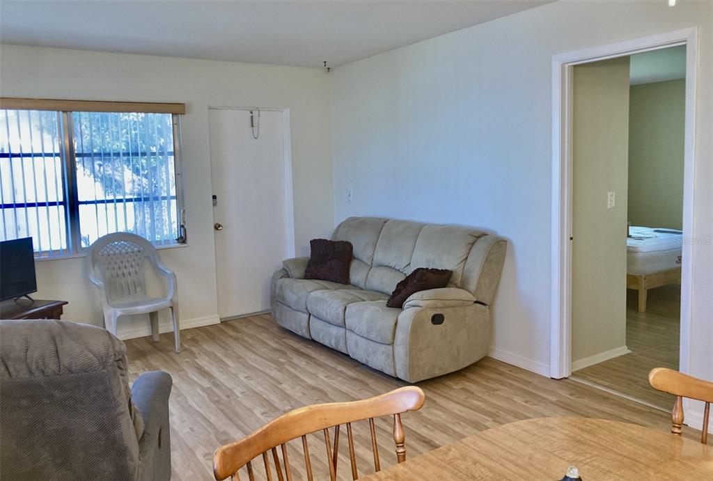 A living room with light wood-look flooring, a beige sofa, and a doorway to a bedroom — 6110 CORAL WAY, BRADENTON, FL