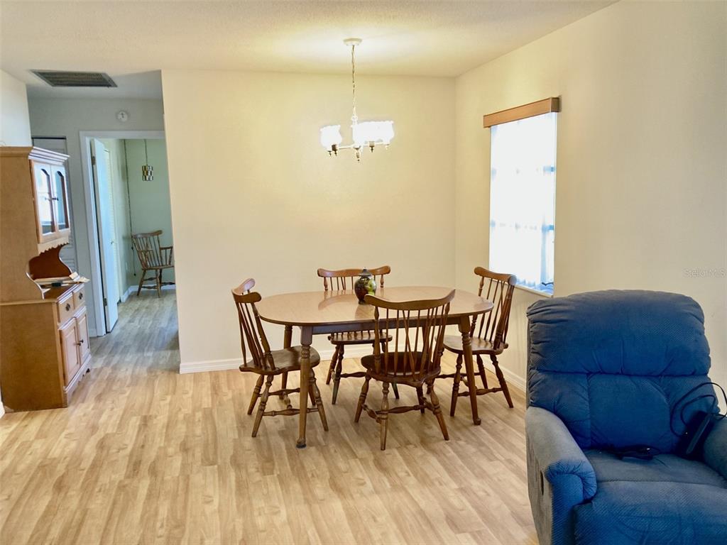 A dining area features a wooden table with chairs, light flooring, and a chandelier — 6110 CORAL WAY, BRADENTON, FL