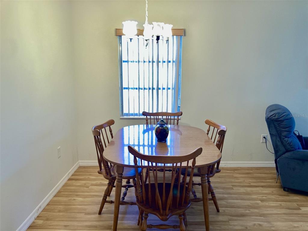 A dining area features a wooden table with four chairs under a chandelier near a window — 6110 CORAL WAY, BRADENTON, FL