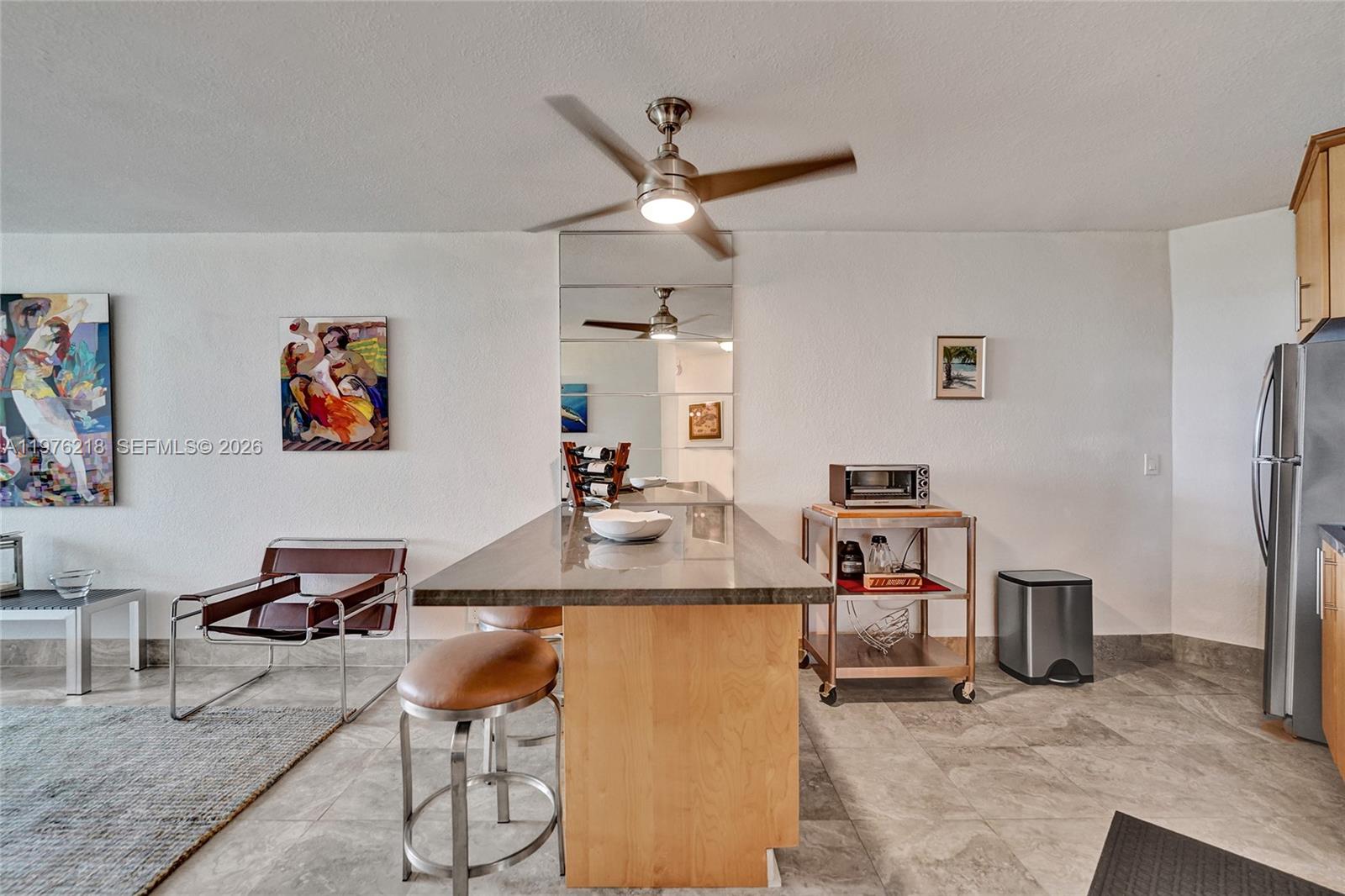 A kitchen island with bar stools sits in a room with tile floors and art — 1936 S Ocean # 20D, Hallandale Beach FL 33009, HALLANDALE BEACH, FL