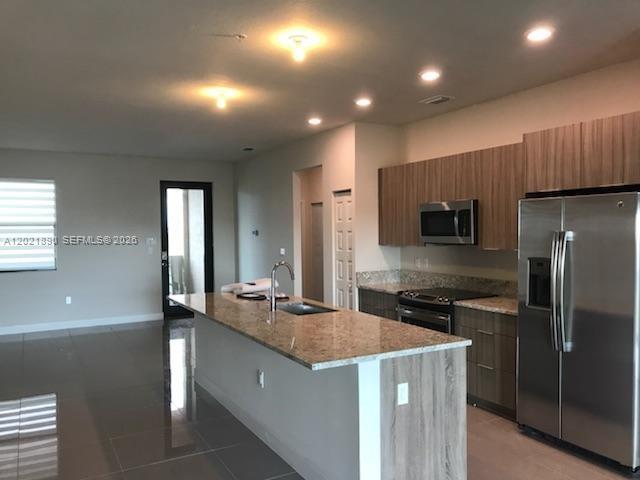A modern kitchen features a granite island, stainless steel appliances, and wood-toned cabinetry — 7805 NW 104 Ave # 31, Doral FL 33178, DORAL, FL