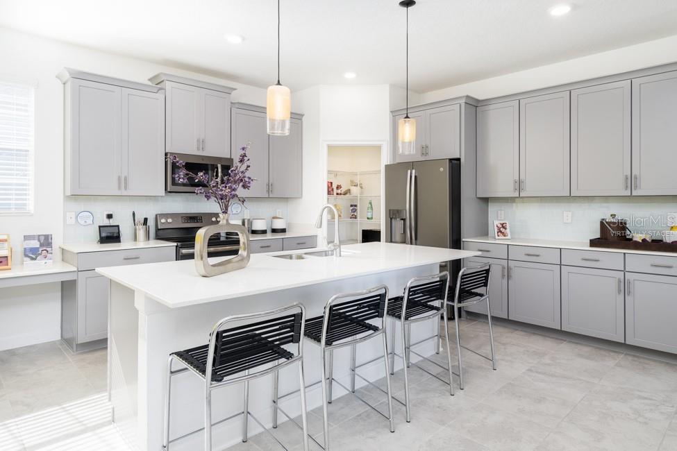 A modern kitchen features gray cabinets, a white island with bar stools, and stainless appliances — 6045 MEDITATION DRIVE, CLERMONT, FL