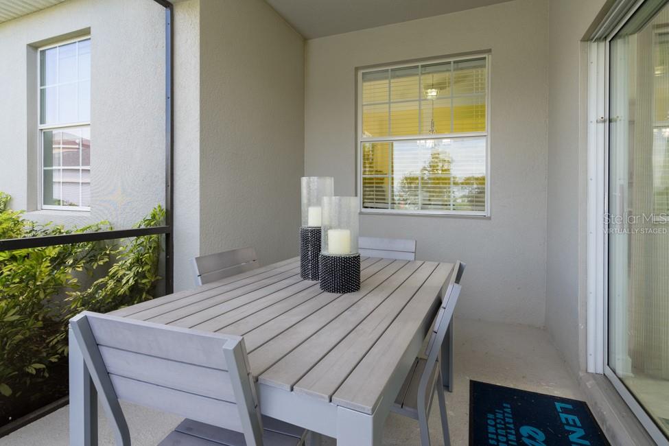 A covered patio features a gray wooden dining table with chairs and two candle centerpieces — 6045 MEDITATION DRIVE, CLERMONT, FL