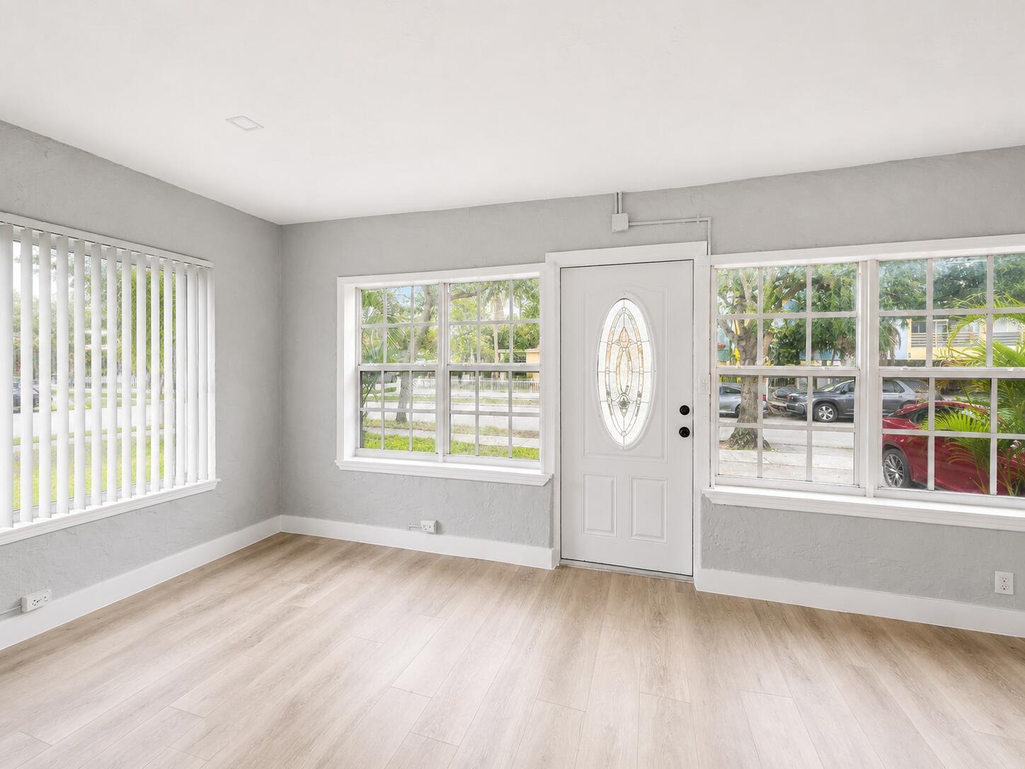 A bright room with light wood-look flooring, gray walls, vertical blinds, and a front door — 1905 Monroe Street, Hollywood FL 33020, HOLLYWOOD, FL