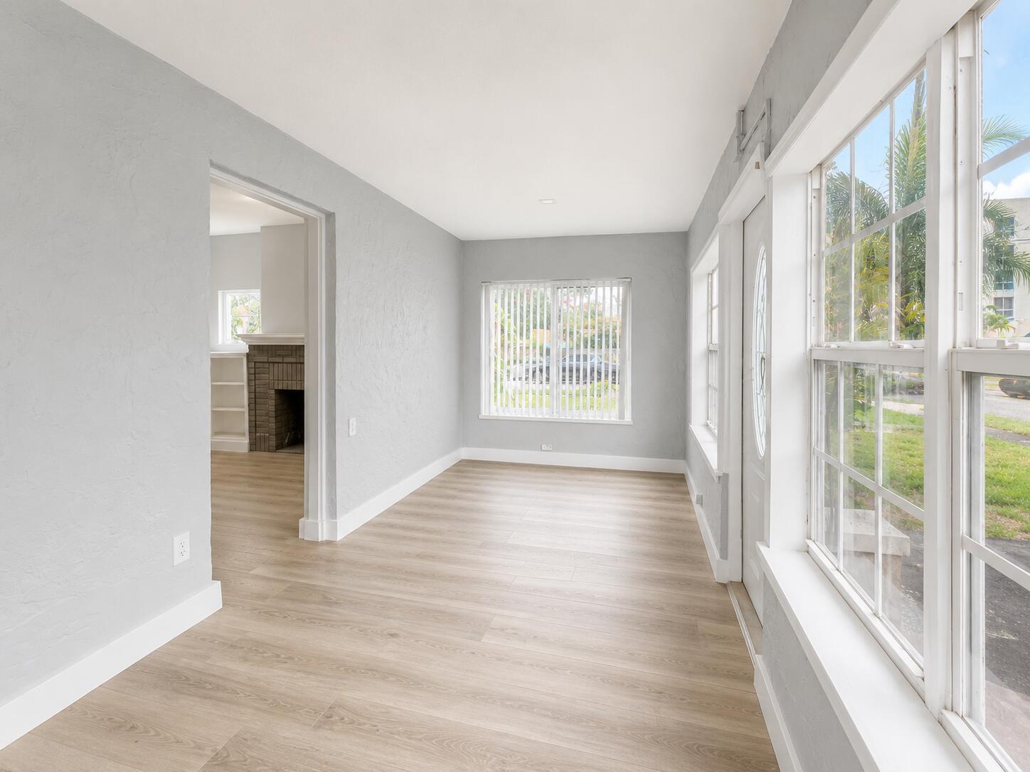A sunroom with light gray walls, wood-look flooring, and large windows looking out onto greenery — 1905 Monroe Street, Hollywood FL 33020, HOLLYWOOD, FL