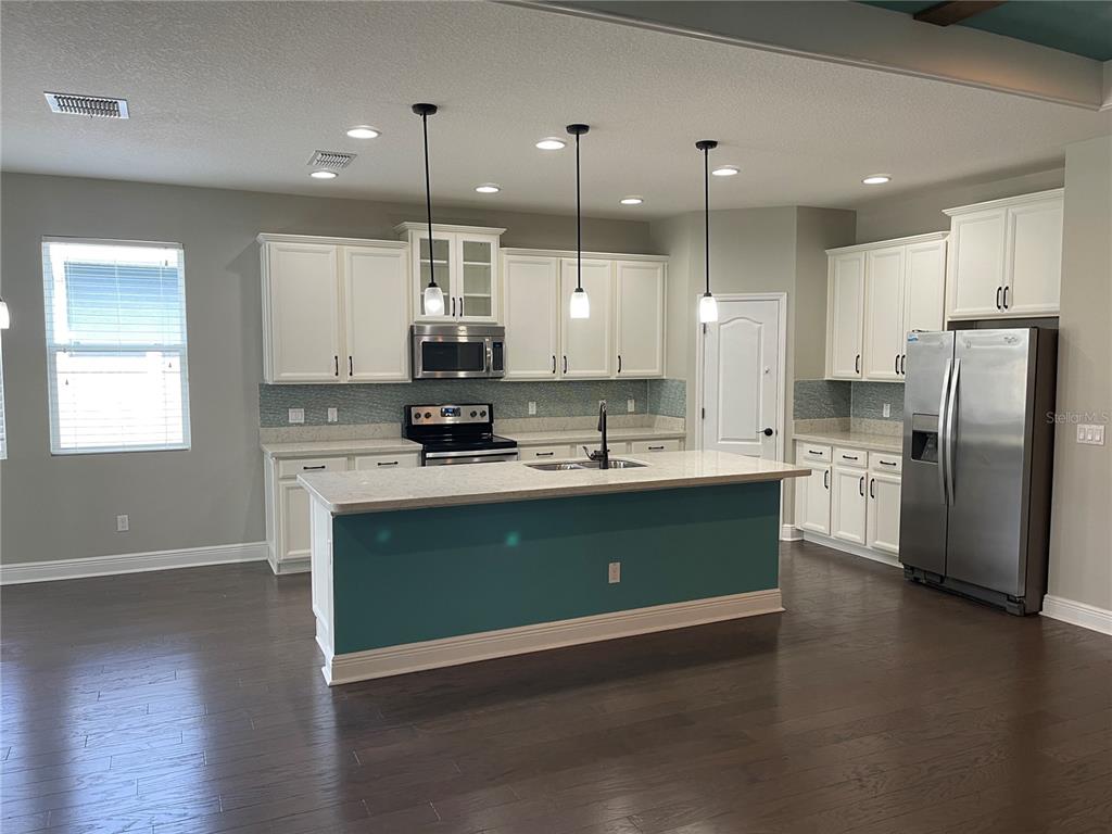 A kitchen features white cabinets, a teal island, stainless steel appliances, and dark wood flooring — 3560 PIXIE LANE, ST CLOUD, FL
