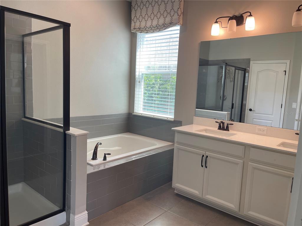 A bathroom features a glass-enclosed shower, a tiled soaking tub, and a white double vanity — 3560 PIXIE LANE, ST CLOUD, FL