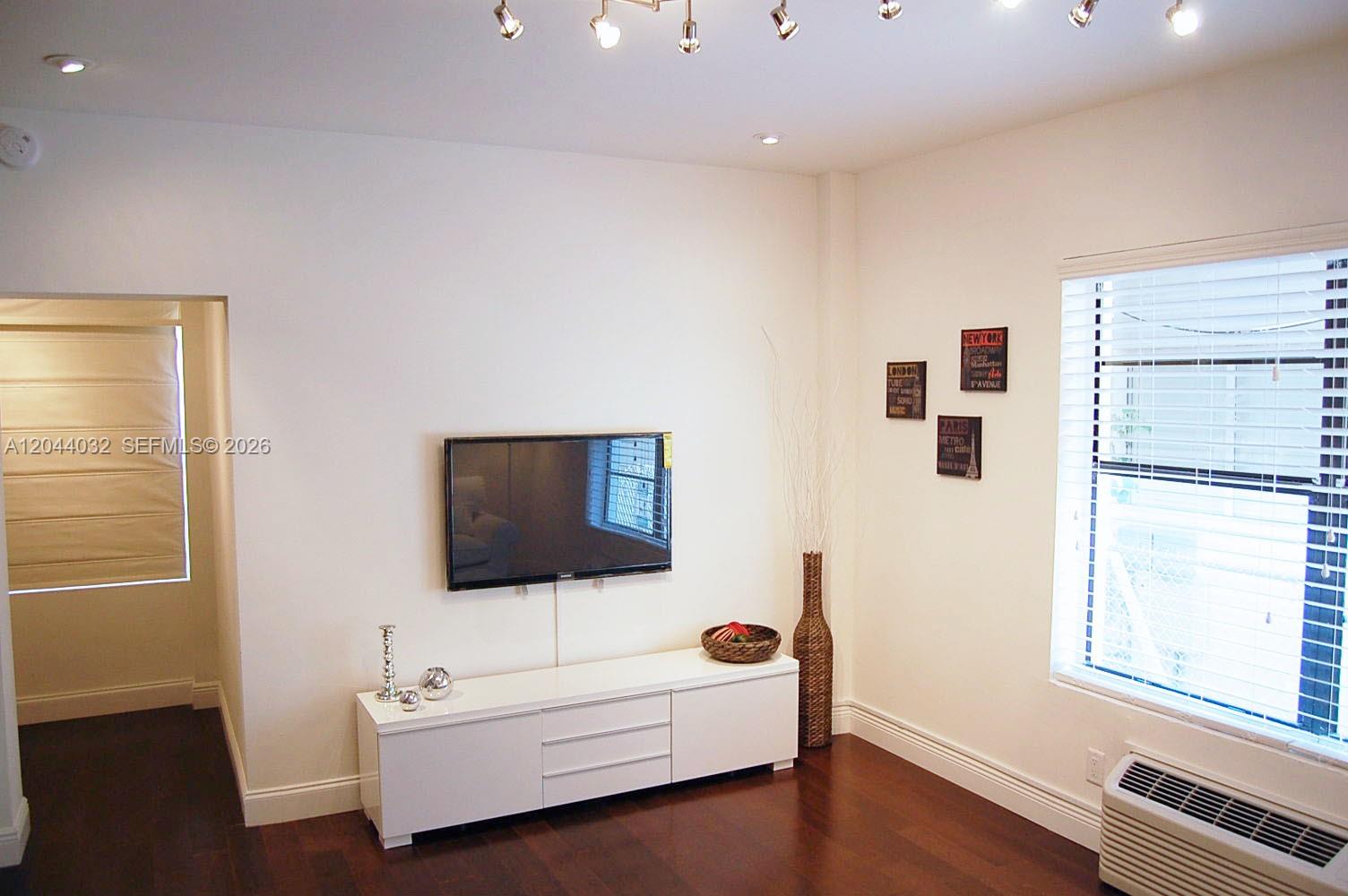 A living room features a wall-mounted television, a white media console, and dark wood flooring — 934 Michigan Ave # 105, Miami Beach FL 33139, MIAMI BEACH, FL