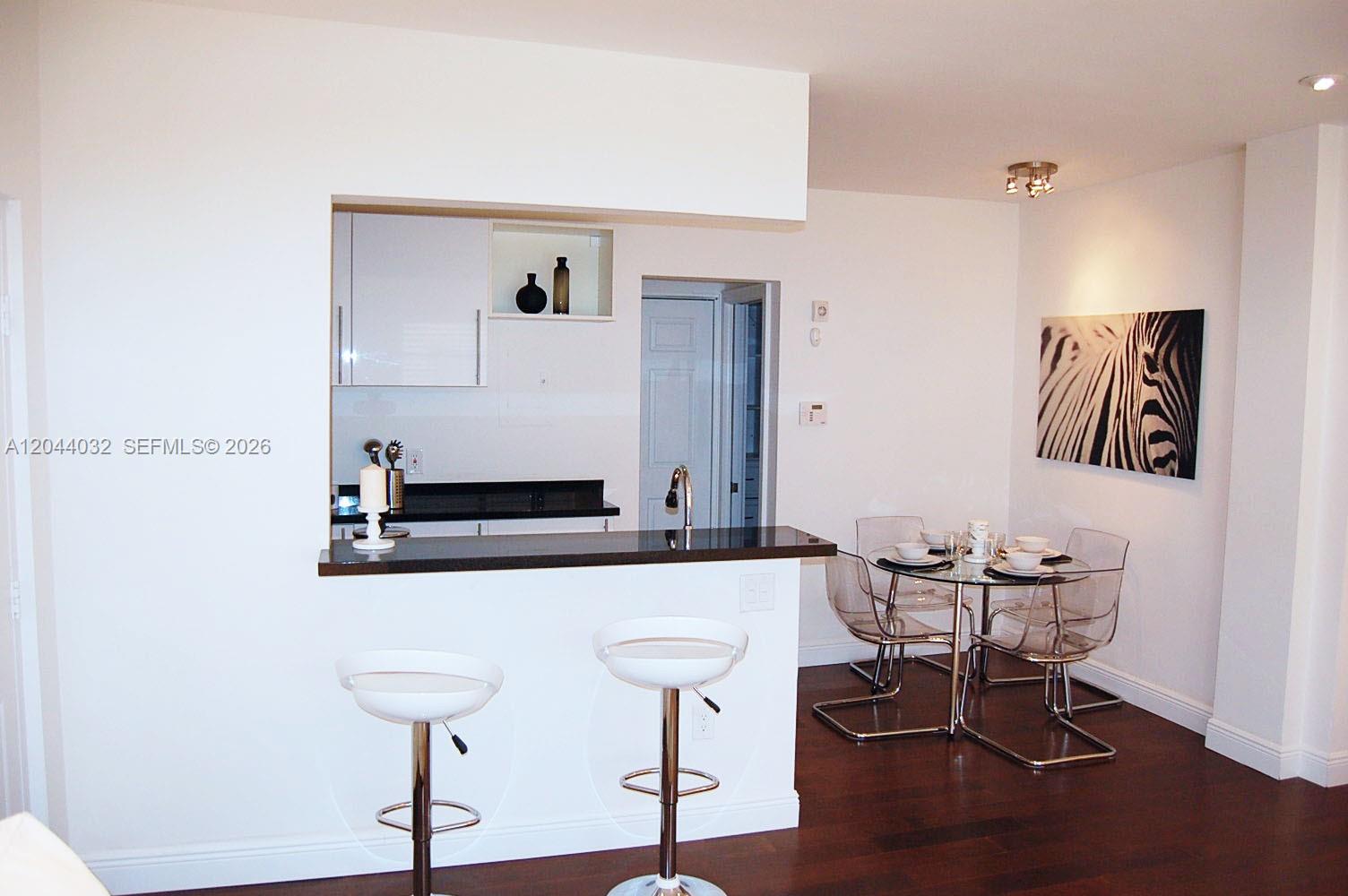 A kitchen with a breakfast bar and stools opens to a dining area with chairs — 934 Michigan Ave # 105, Miami Beach FL 33139, MIAMI BEACH, FL