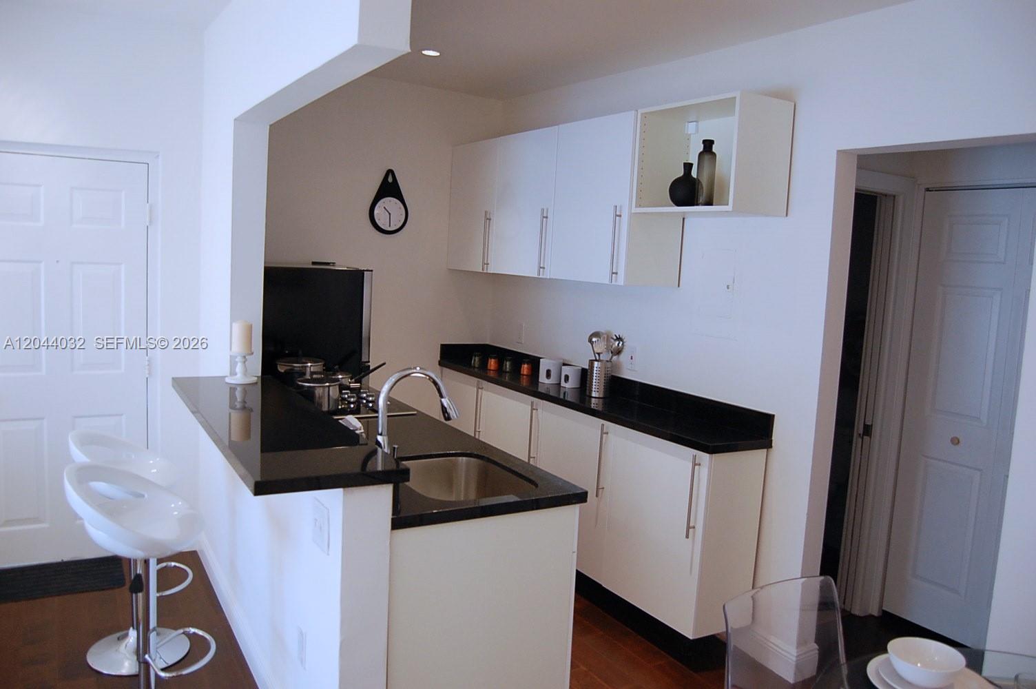 A kitchen features white cabinets, black countertops, a stainless steel sink, and a breakfast bar — 934 Michigan Ave # 105, Miami Beach FL 33139, MIAMI BEACH, FL