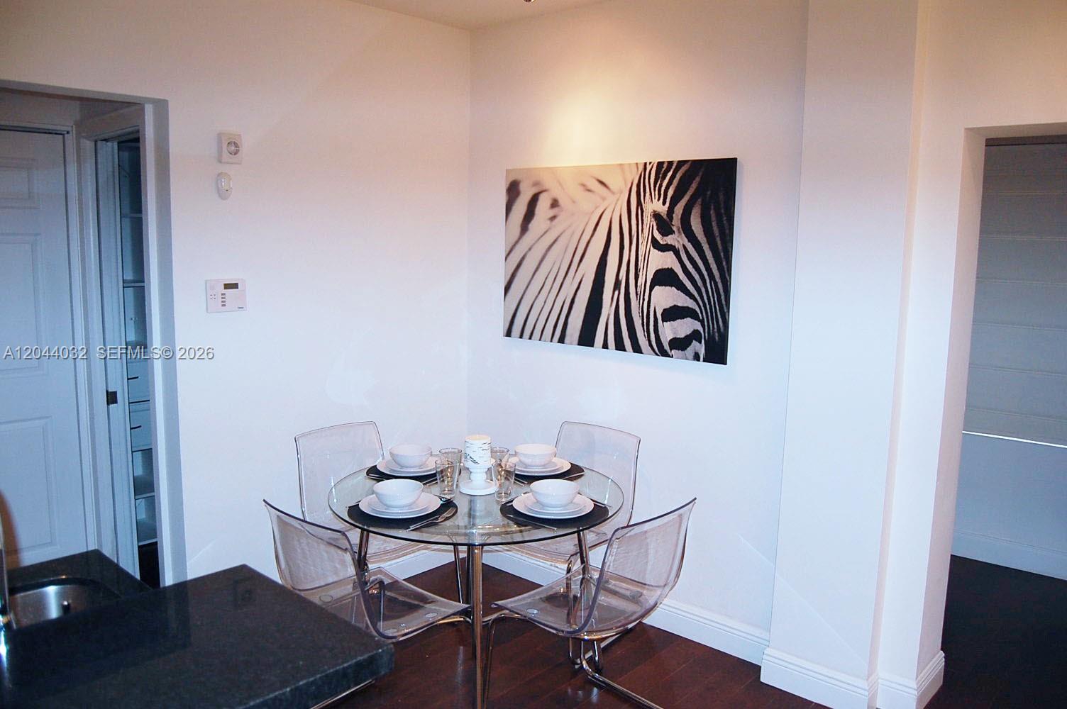 A dining area features a glass table with four clear chairs and zebra wall art — 934 Michigan Ave # 105, Miami Beach FL 33139, MIAMI BEACH, FL