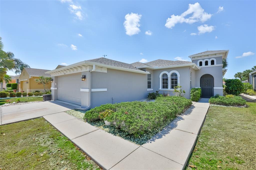 A gray single-story house with a two-car garage, arched windows, and a landscaped front yard — 448 NOBLE FAIRE DRIVE, SUN CITY CENTER, FL