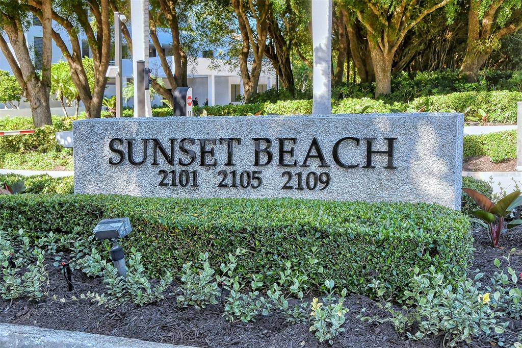 A stone monument sign displays the words Sunset Beach and the numbers 2101, 2105, 2109 — 2109 GULF OF MEXICO DRIVE UNIT 1203, LONGBOAT KEY, FL