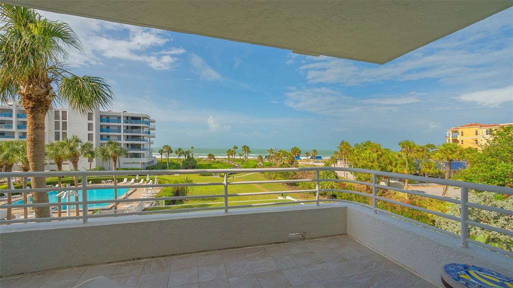 A balcony with white railings overlooks a swimming pool, green lawn, and the ocean — 2109 GULF OF MEXICO DRIVE UNIT 1203, LONGBOAT KEY, FL