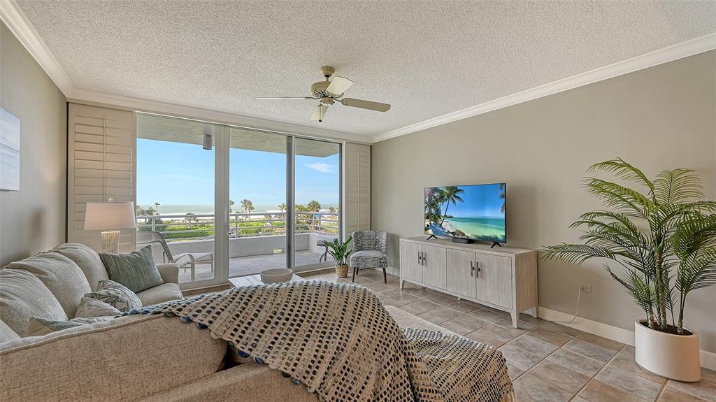 A living room features a beige sofa, a television on a cabinet, and a balcony view — 2109 GULF OF MEXICO DRIVE UNIT 1203, LONGBOAT KEY, FL