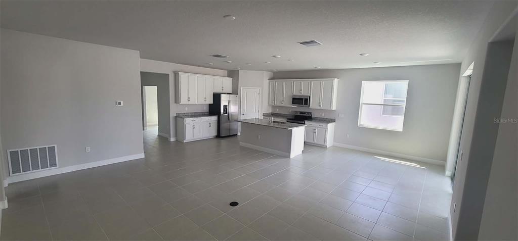 An open-concept kitchen features white cabinetry, granite countertops, a center island, and light tile flooring — 9273 HIGHLAND HILLS DRIVE, HUDSON, FL