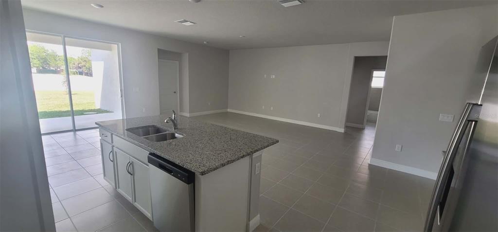 A kitchen island with a granite countertop and stainless steel dishwasher faces an open living area — 9273 HIGHLAND HILLS DRIVE, HUDSON, FL