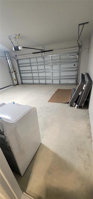 A garage with a concrete floor, a white washing machine, and a metal sectional door — 9273 HIGHLAND HILLS DRIVE, HUDSON, FL