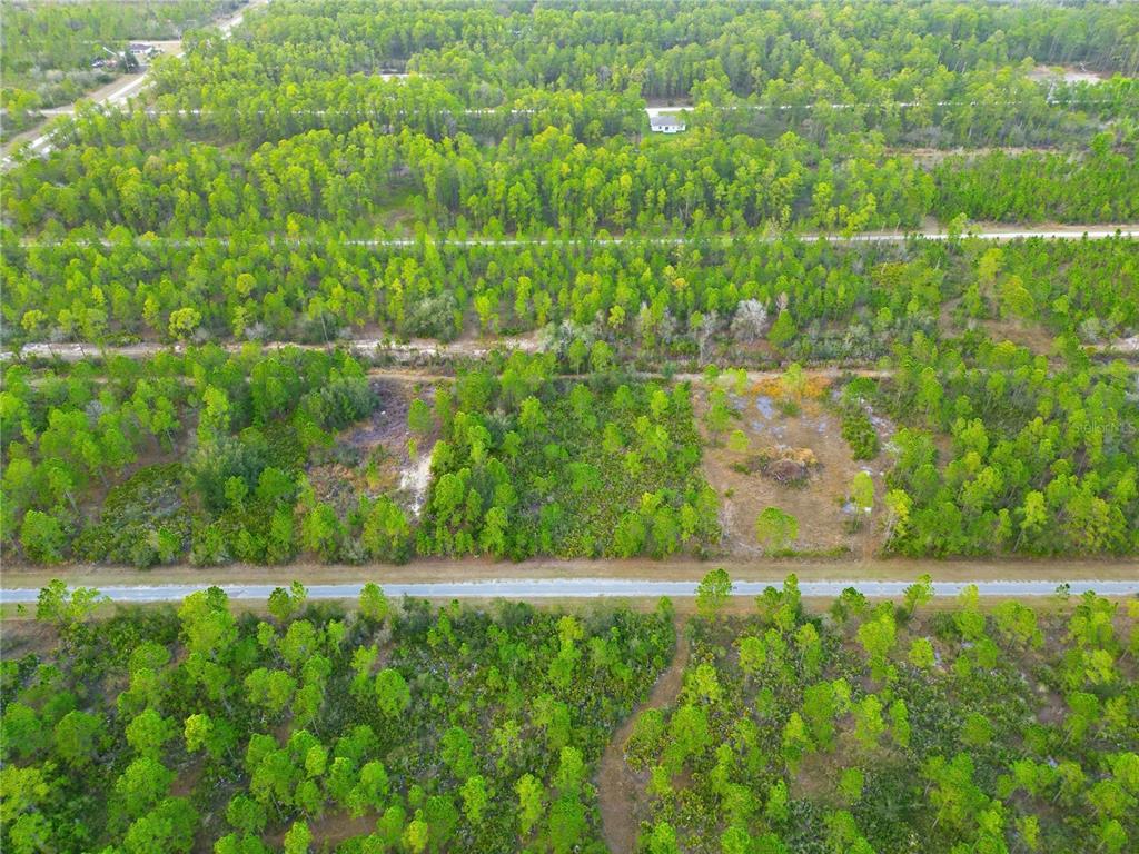 An aerial view shows a paved road running through a wooded area with cleared lots — 310 TROPICANA DRIVE, INDIAN LAKE ESTATES, FL