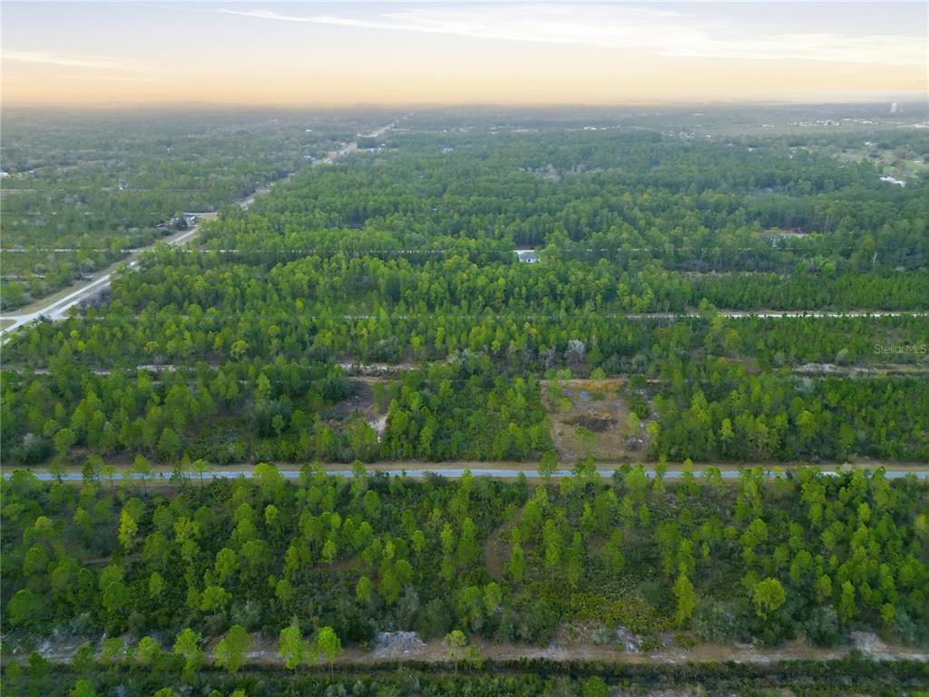 An aerial view shows a wooded landscape with several paved roads running through the trees — 310 TROPICANA DRIVE, INDIAN LAKE ESTATES, FL