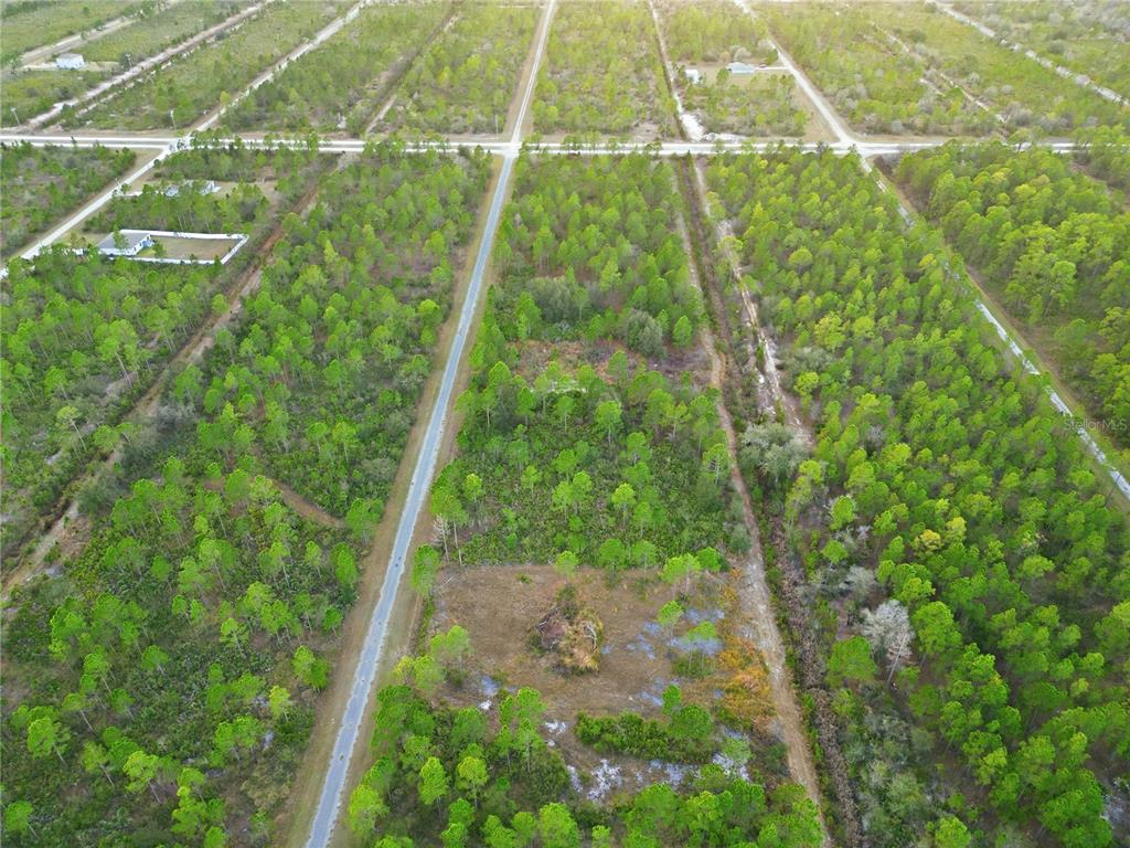 An aerial view shows a rectangular, wooded plot of land bordering a paved road — 310 TROPICANA DRIVE, INDIAN LAKE ESTATES, FL