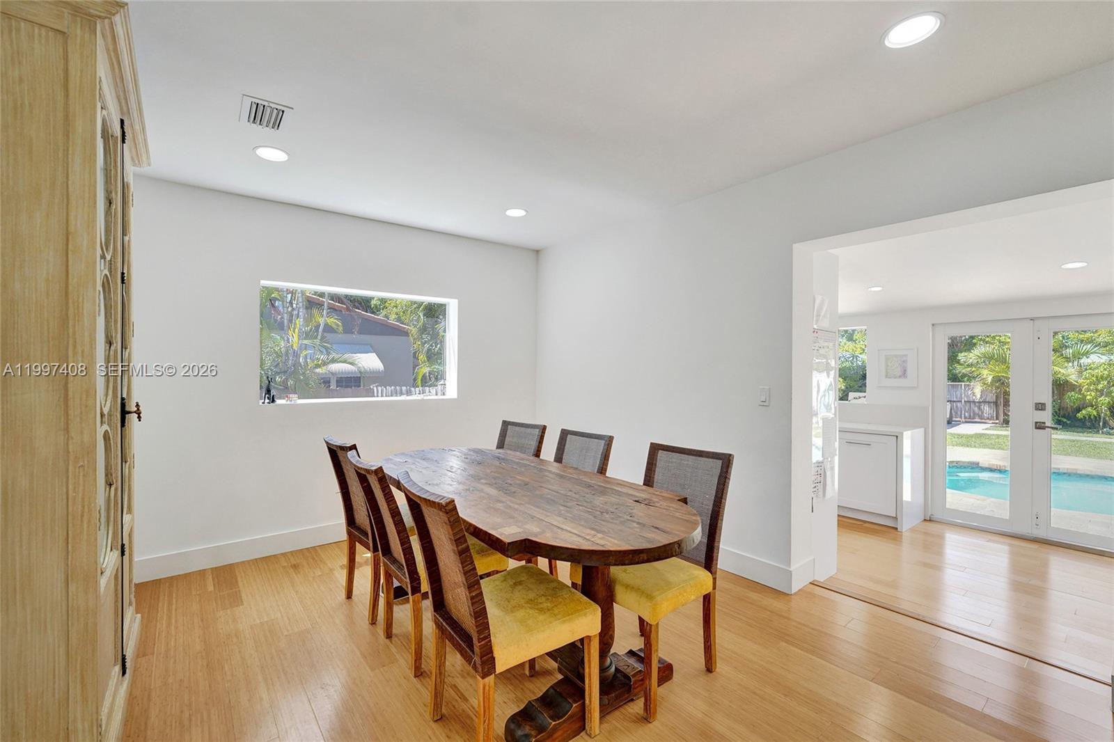 A dining room features a wooden table, upholstered chairs, light wood flooring, and a pool view — 1515 Dewey St, Hollywood FL 33020, HOLLYWOOD, FL
