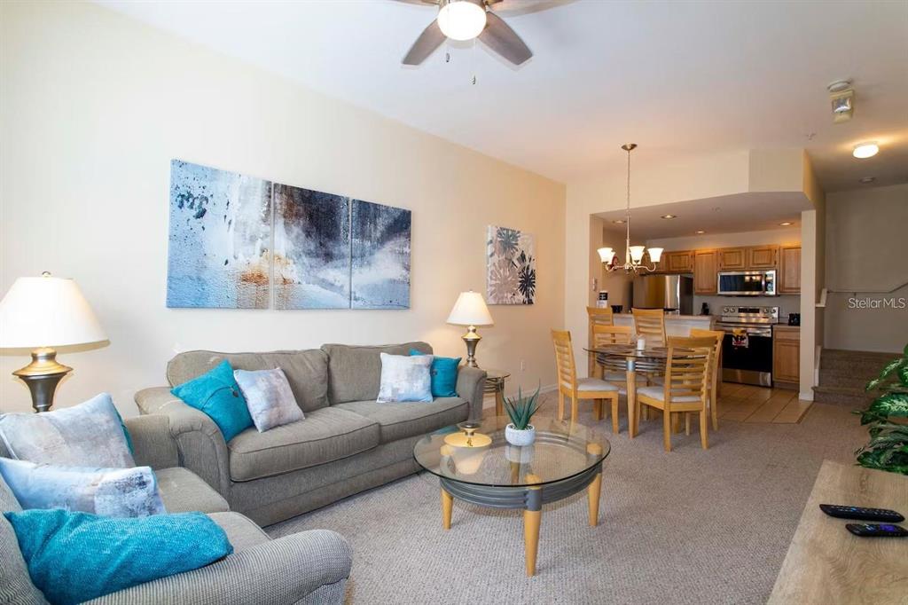 A living room with a gray sofa and glass coffee table opens to a dining area — 4011 VENETIAN BAY DRIVE UNIT 106, KISSIMMEE, FL