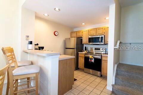 A kitchen features light wood cabinets, stainless steel appliances, and a breakfast bar with stools — 4011 VENETIAN BAY DRIVE UNIT 106, KISSIMMEE, FL