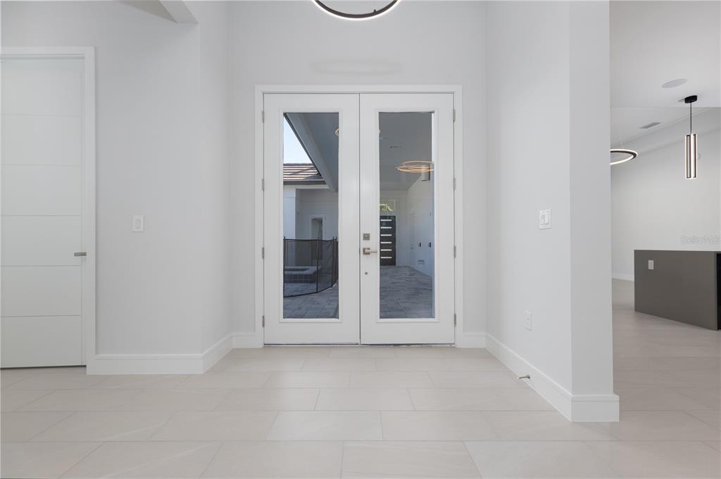 A bright entryway features white walls, light tile flooring, and double glass doors leading outside — 109 NEW LEATHERWOOD DRIVE, PALM COAST, FL