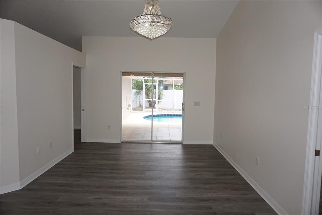 A room with gray wood-look flooring, a crystal chandelier, and sliding doors leading to a pool — 6708 66TH AVENUE E, BRADENTON, FL