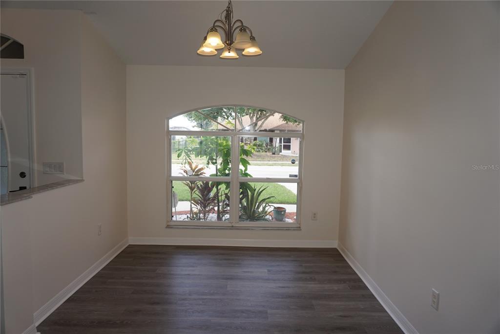 An empty dining area features wood-look flooring, a central chandelier, and a large arched window — 6708 66TH AVENUE E, BRADENTON, FL